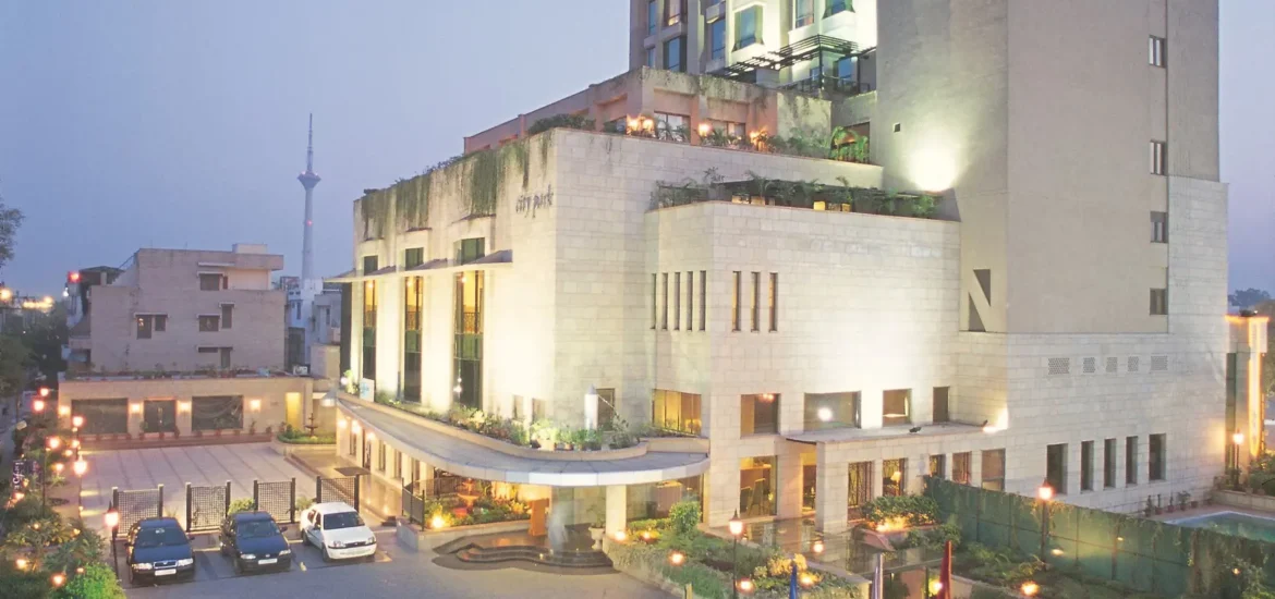 Exterior view of Hotel City Park Pitampura with illuminated modern architecture, landscaped entrance, and decorative lighting at dusk.