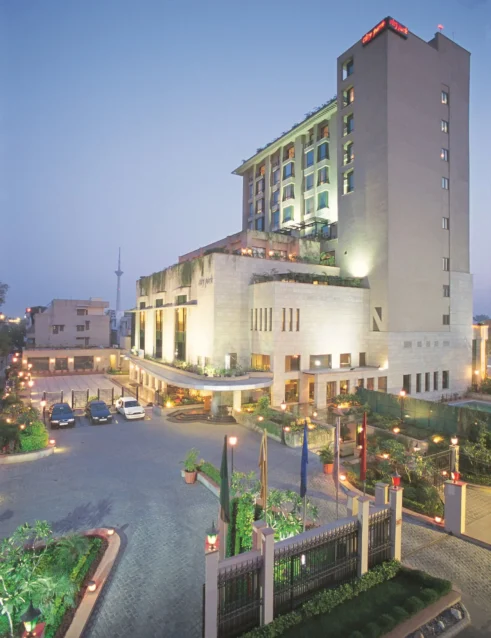 Exterior view of Hotel City Park Pitampura with illuminated modern architecture, landscaped entrance, and decorative lighting at dusk.