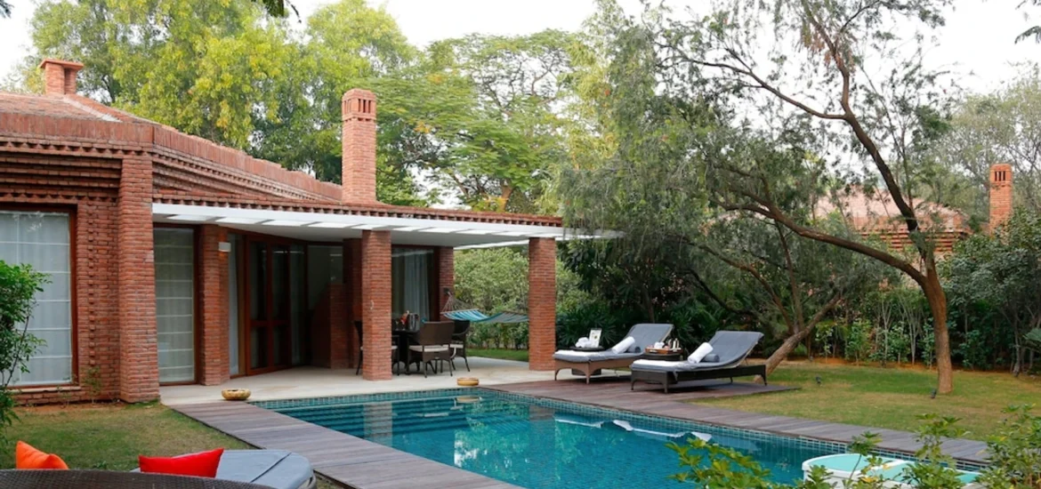 Modern luxury villa with a private swimming pool, outdoor lounge seating, and lush greenery in a peaceful setting.