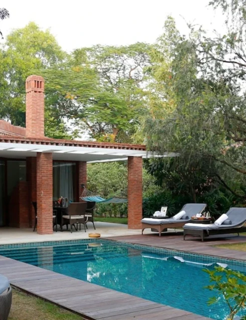 Modern luxury villa with a private swimming pool, outdoor lounge seating, and lush greenery in a peaceful setting.